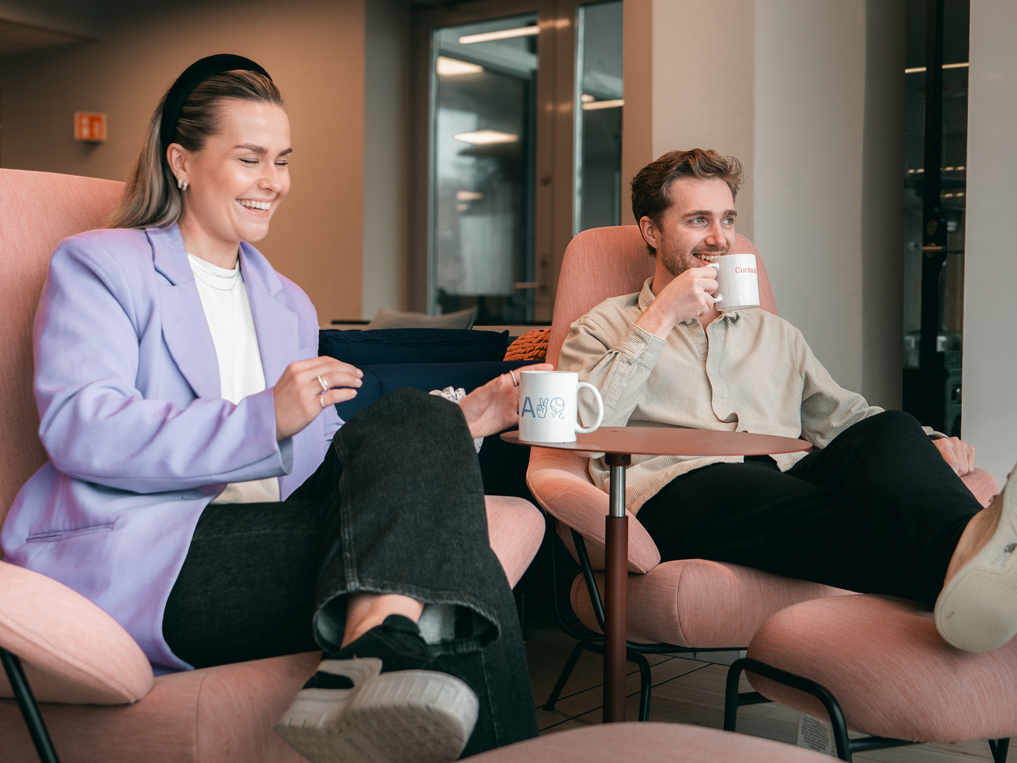 To konsulenter som sitter og smiler med kaffekoppen i hånda. Foto